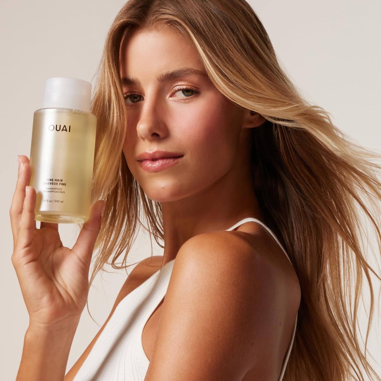 Model looks at camera and holds OUAI fine hair cheveux fns shampoo