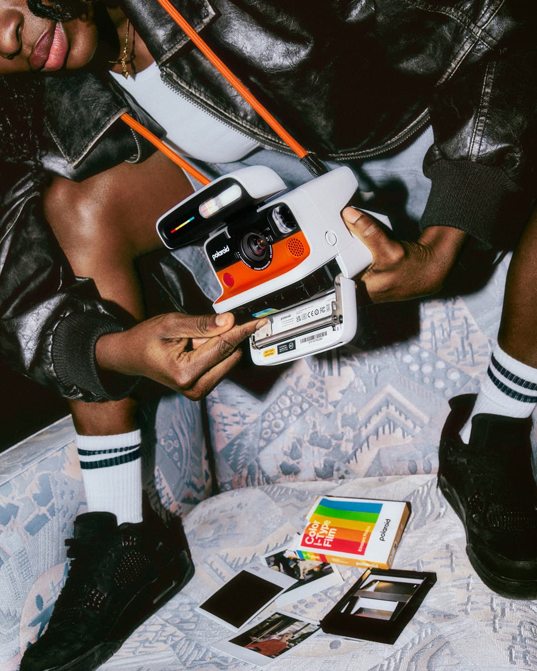 A person is holding an orange Polaroid Flip camera while inserting a new instant film pack.