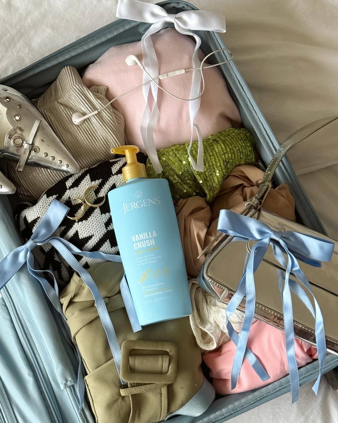 Suitcase full of travel necessities like clothes, headphones, and Jergens Vanilla Crush