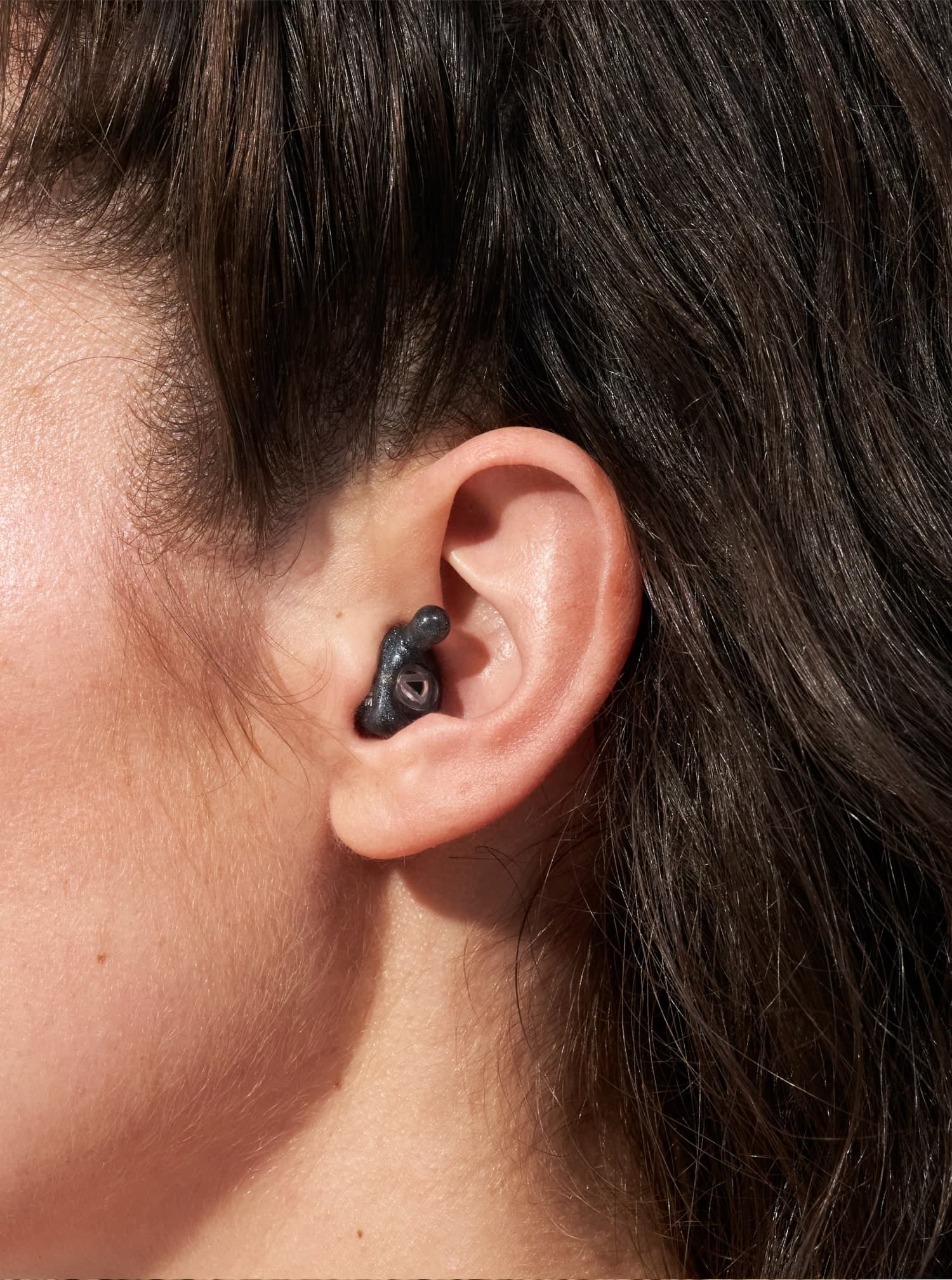 A close-up of a person's ear with an Alpine earplug placed in.