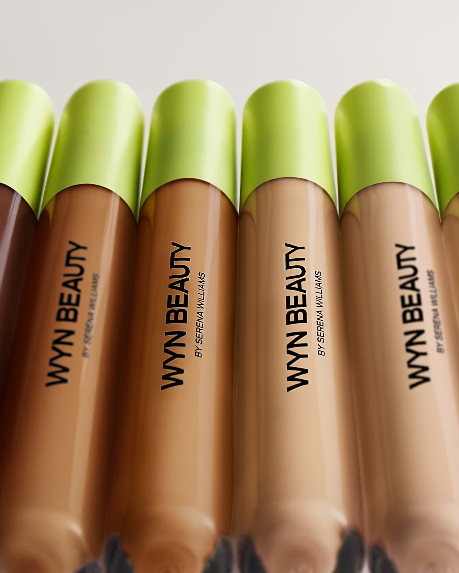 Five tubes of WYN BEAUTY cosmetics with lime green caps, featuring different shades, arranged closely together on a plain background.