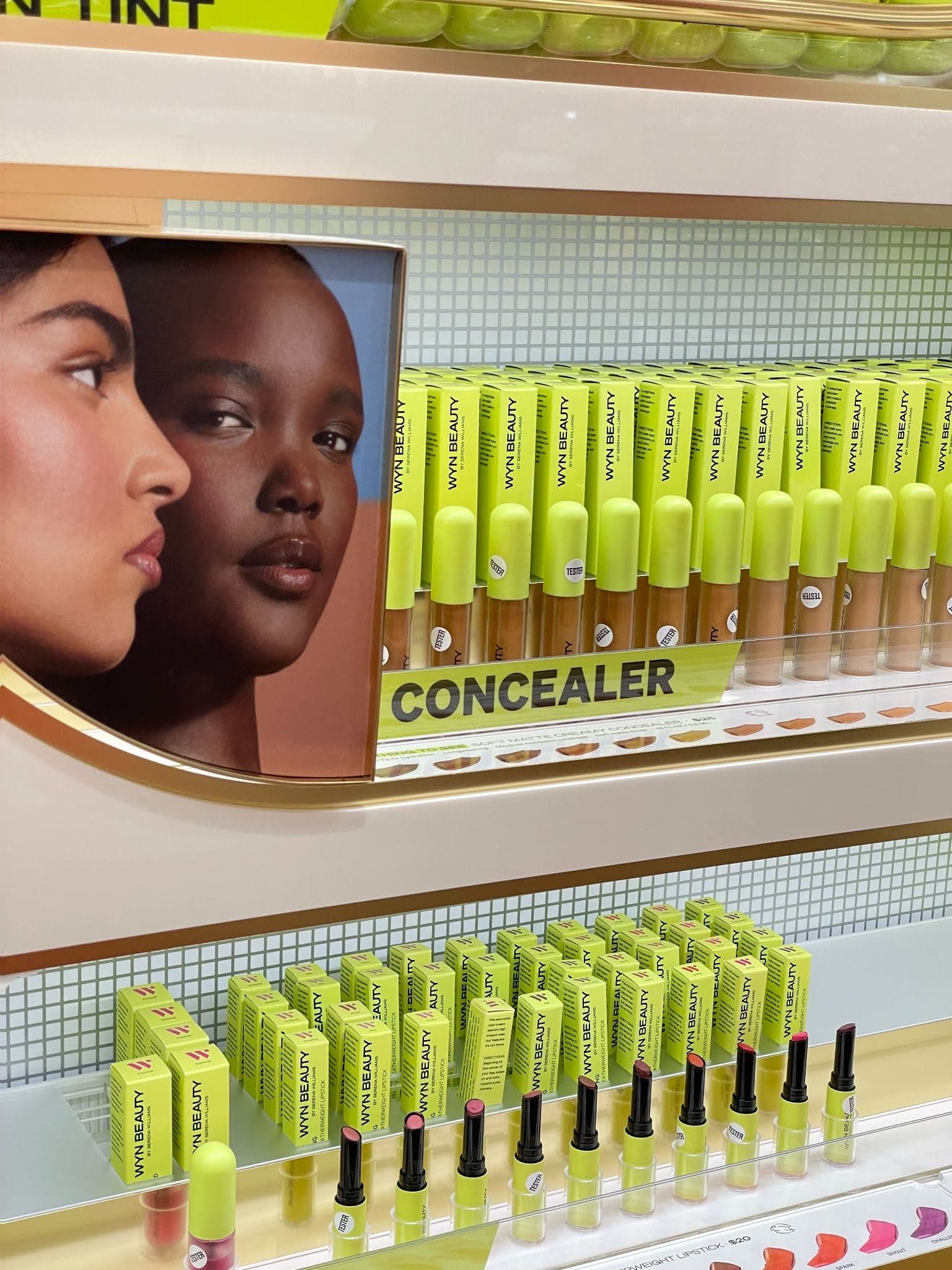 A display of WYN Beauty concealers and lipsticks, featuring diverse models, with bright lime green packaging arranged neatly on shelves.