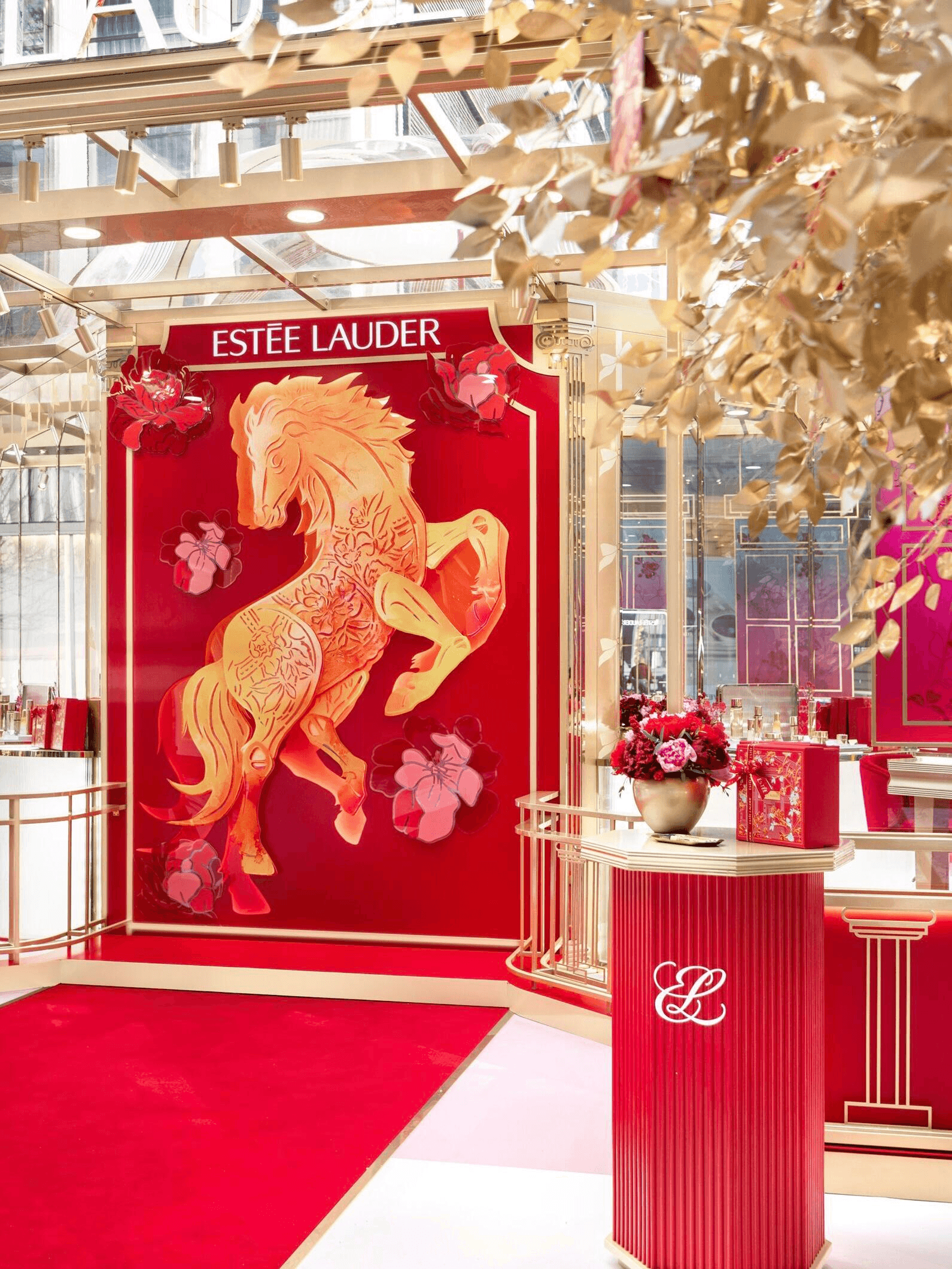Luxurious Estee Lauder display with a vibrant golden horse design and floral accents on a red backdrop, adorned with elegant gold detailing.