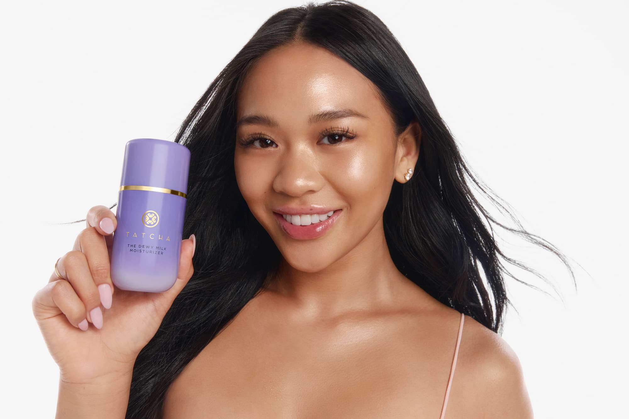 Olympian Suni Lee is holding a Tatcha Dewy Milk bottle in front of a bright white background