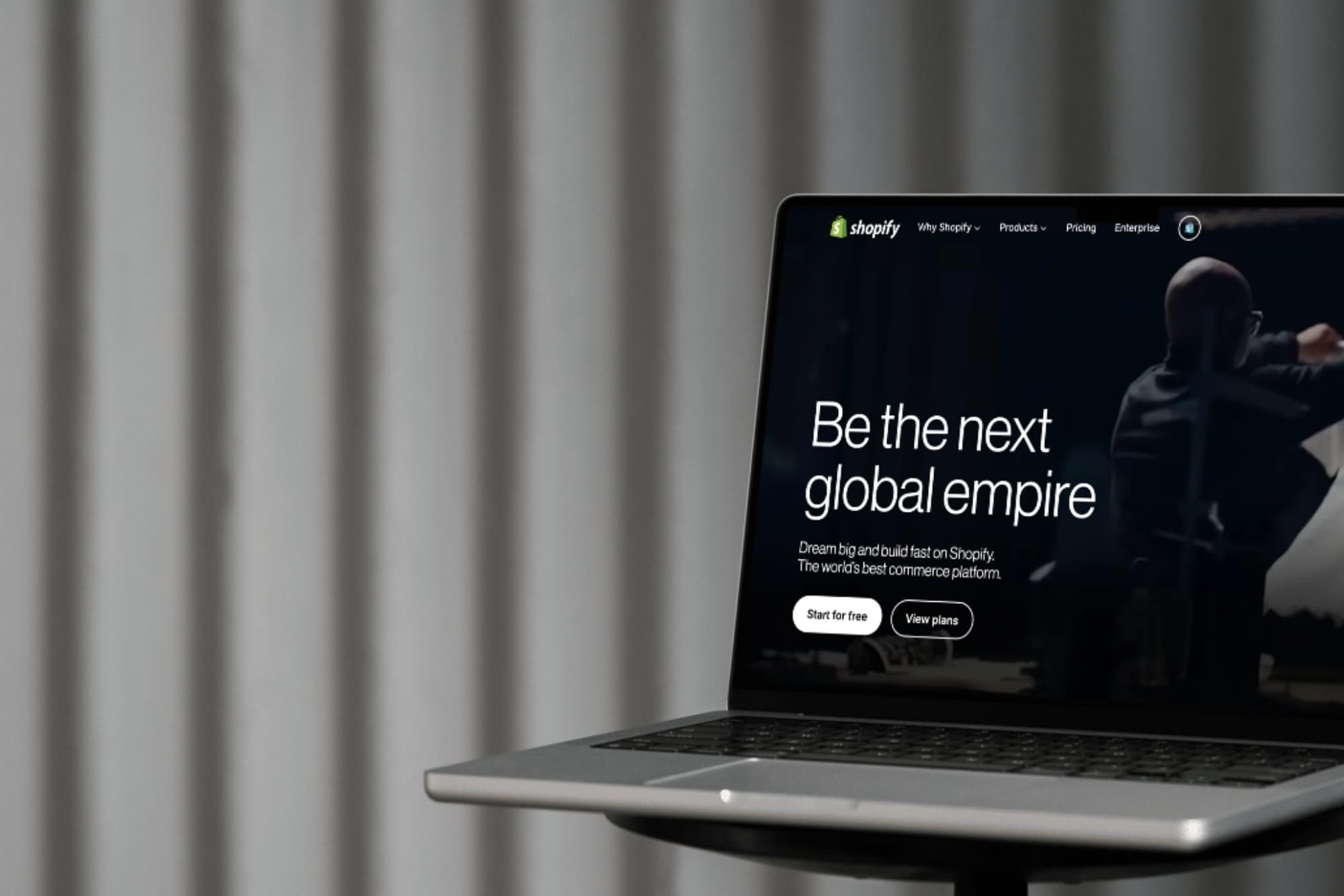 Laptop screen displaying Shopify's homepage with text "Be the next global empire" and options to start for free or view plans.