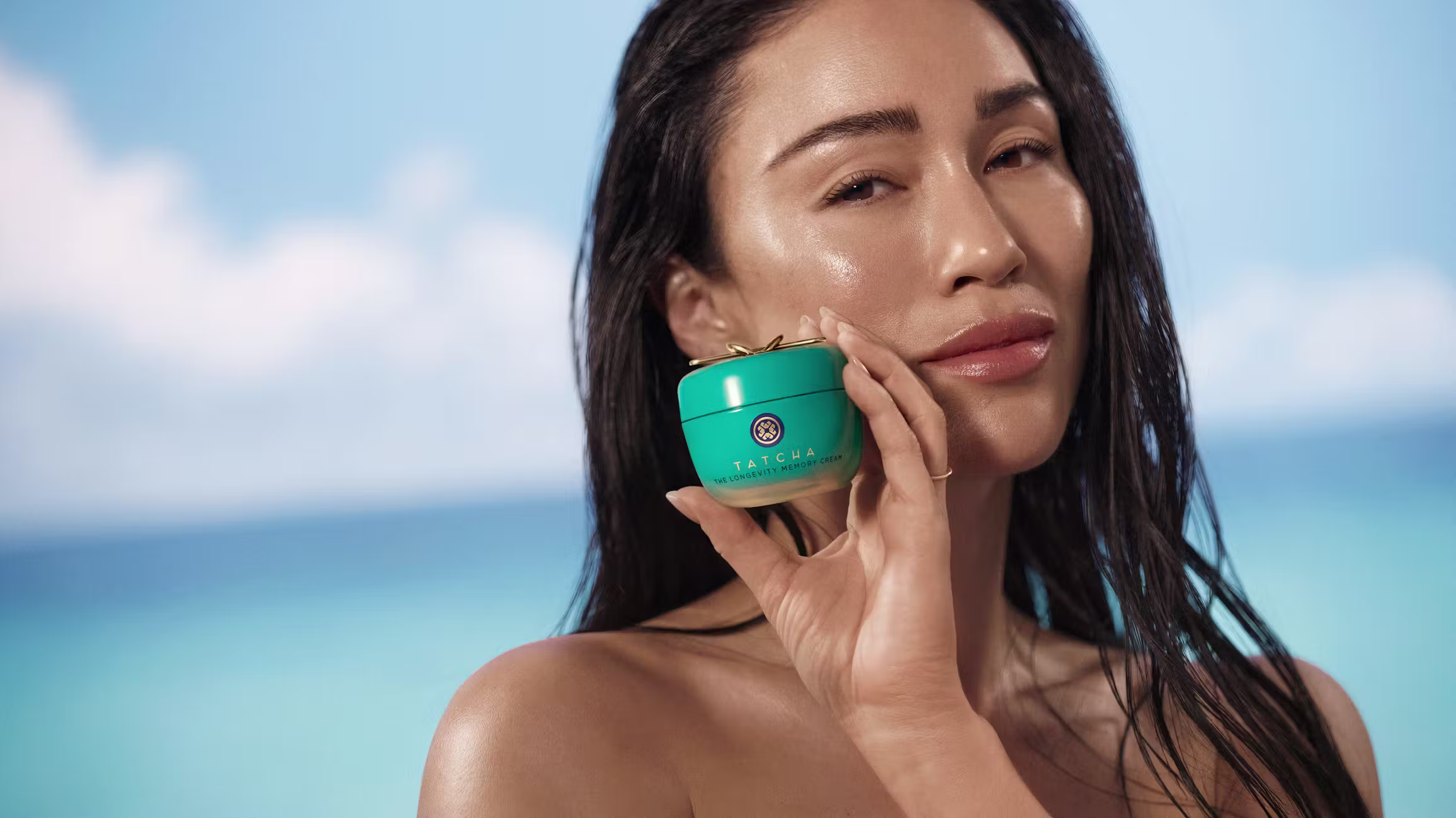 Models looks into the camera holding Tatcha's memory cream up to her face