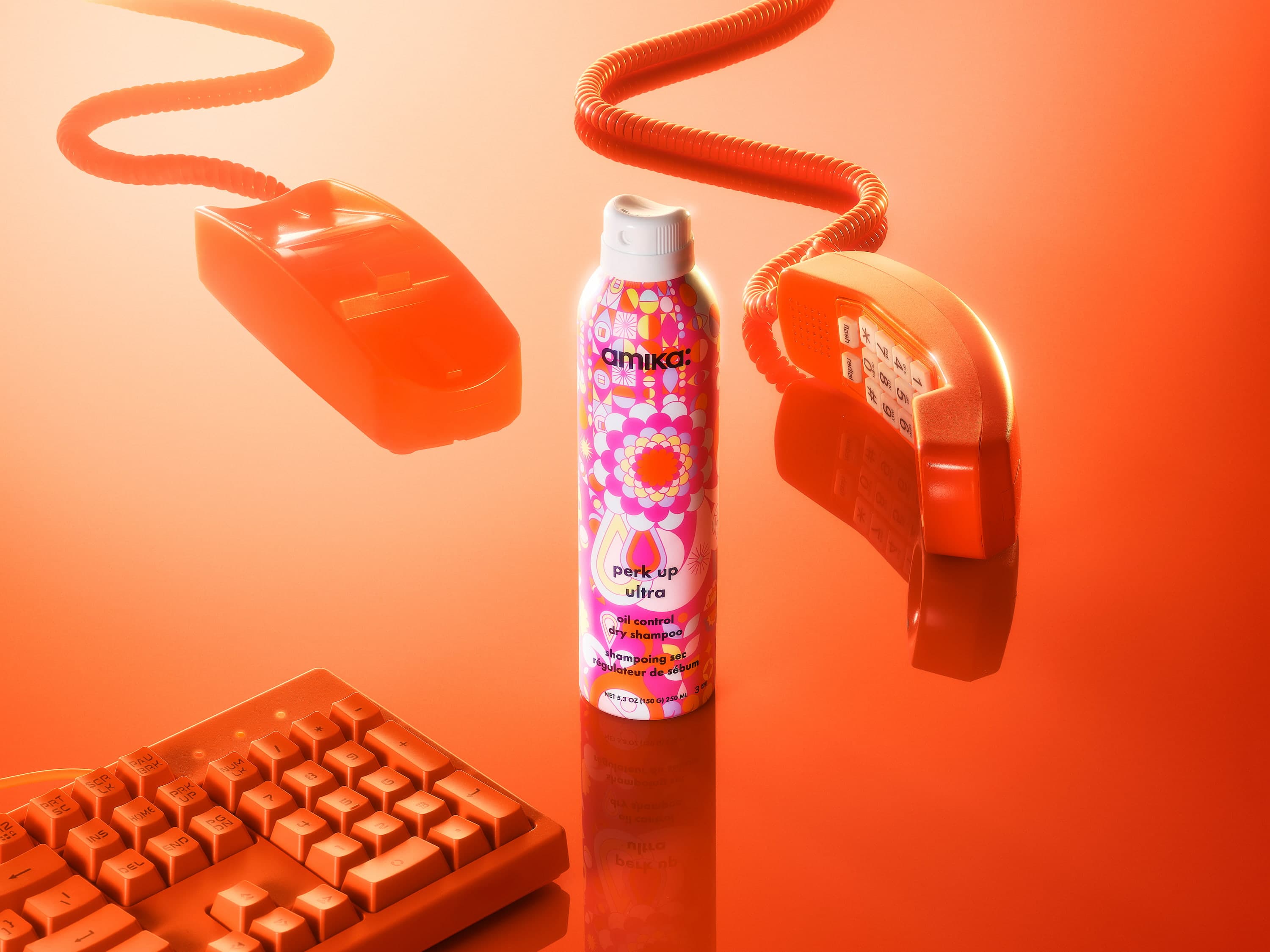 A pink and orange can of Amika dry shampoo sits among orange retro technology, including a telephone, computer mouse, and keyboard.