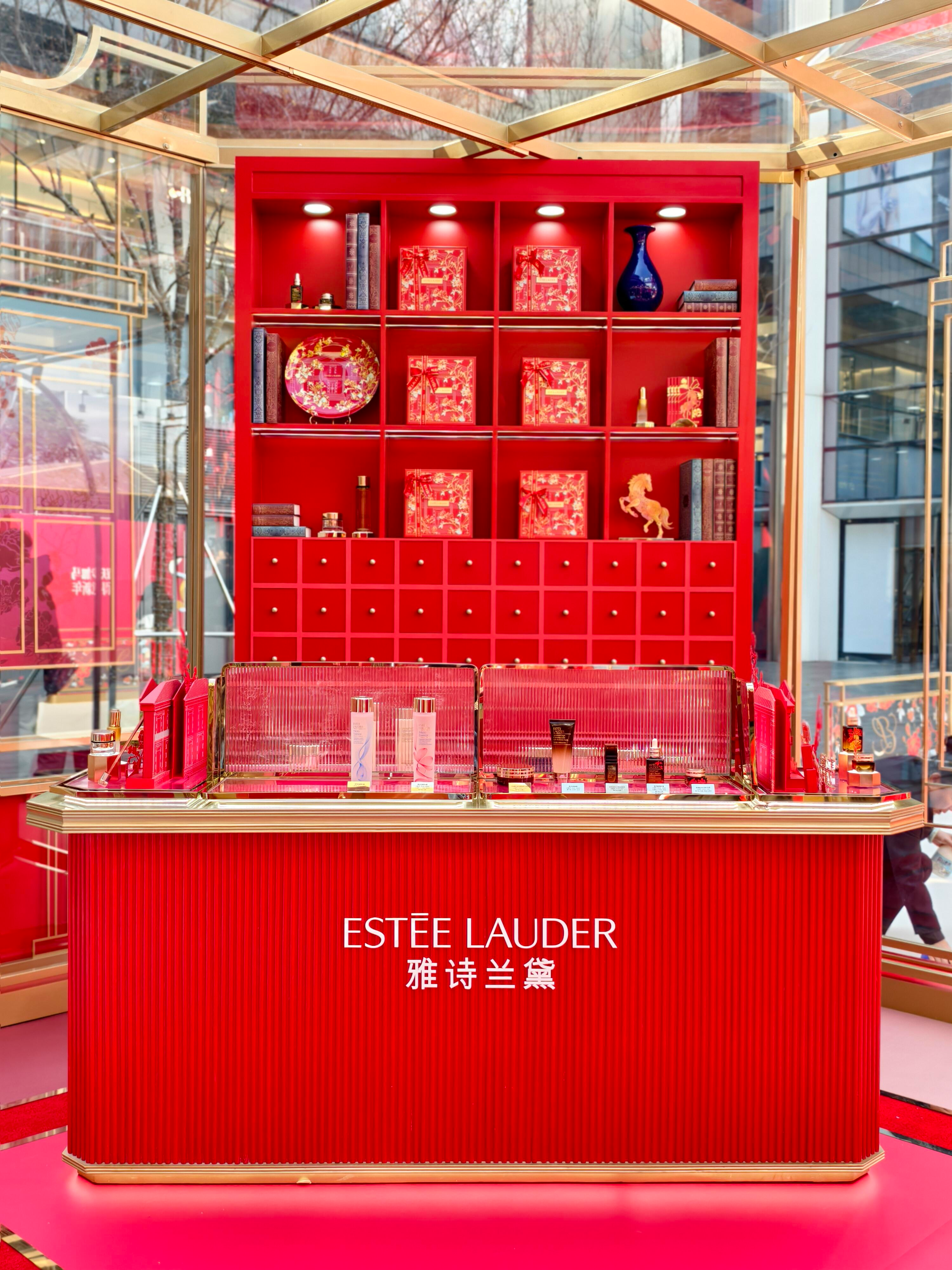 Red Estee Lauder display with skincare products, ornate shelves, and decorative items in a well-lit store.