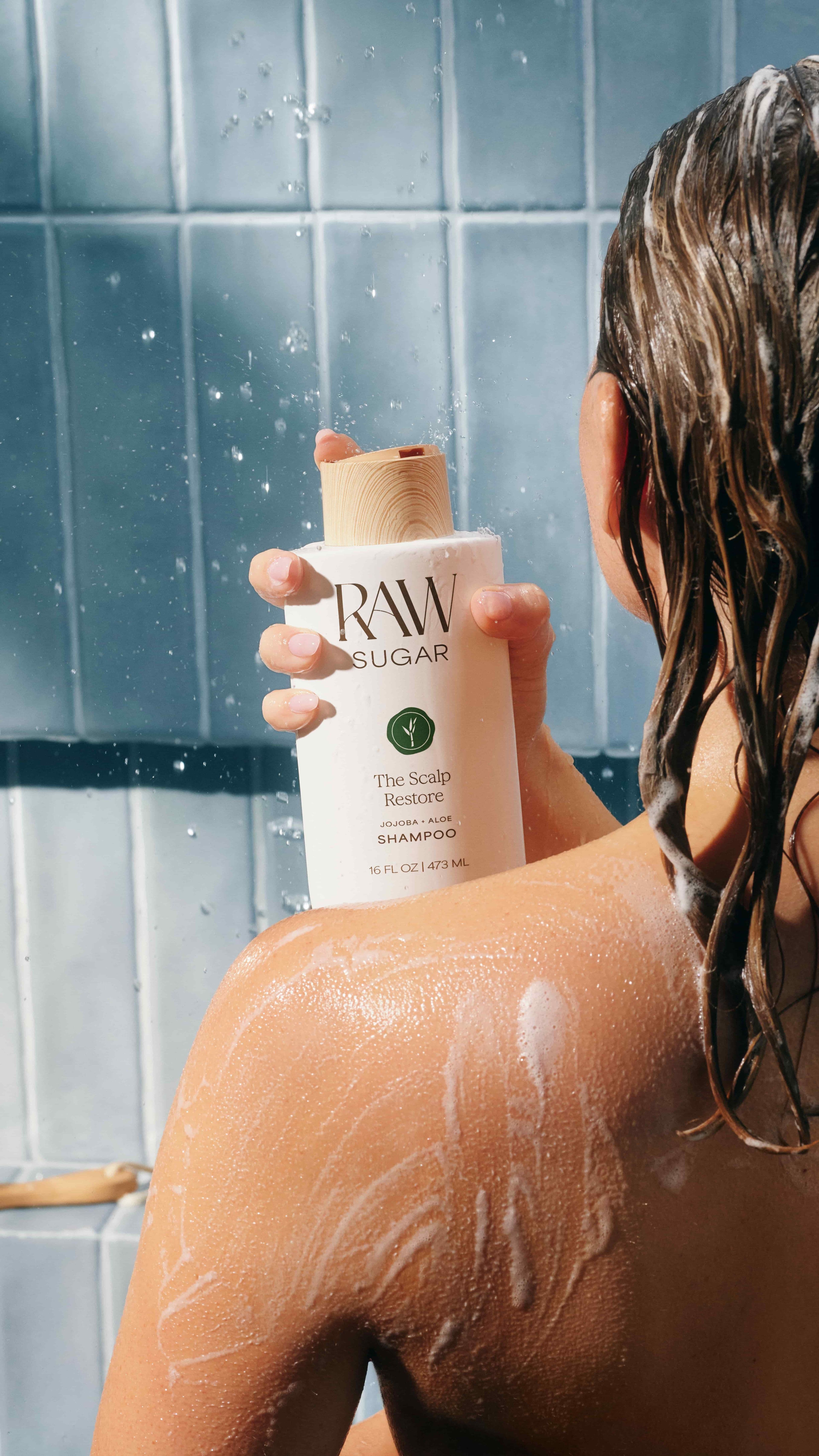 Close up of model in the shower holding Raw Sugar scalp restore shampoo
