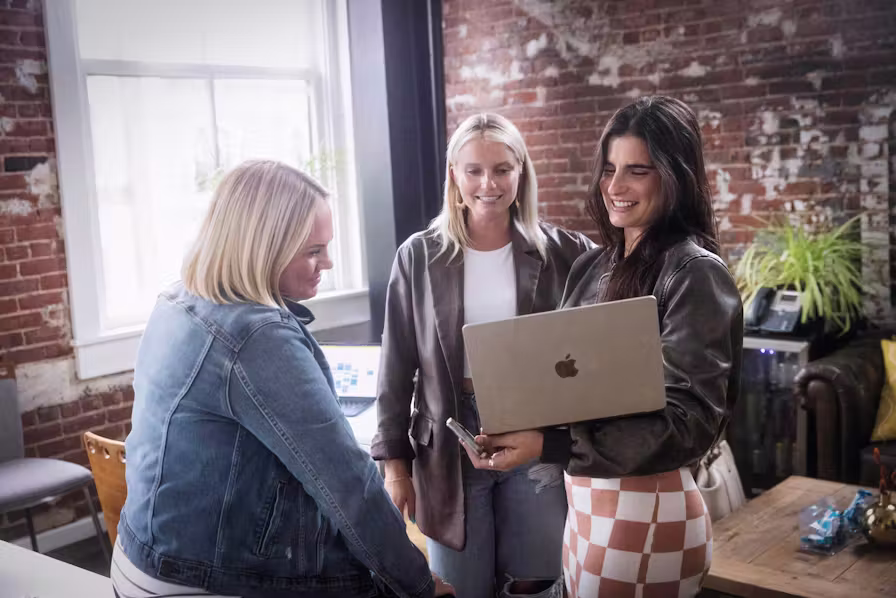 three team members smile around a laptop, looking at a project