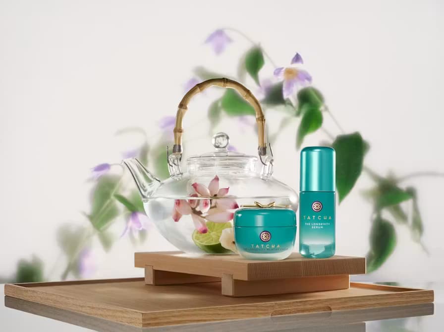 A Japanese tea set with Tatcha's longevity memory cream, on top of a nice wooden piece with flowers in the background