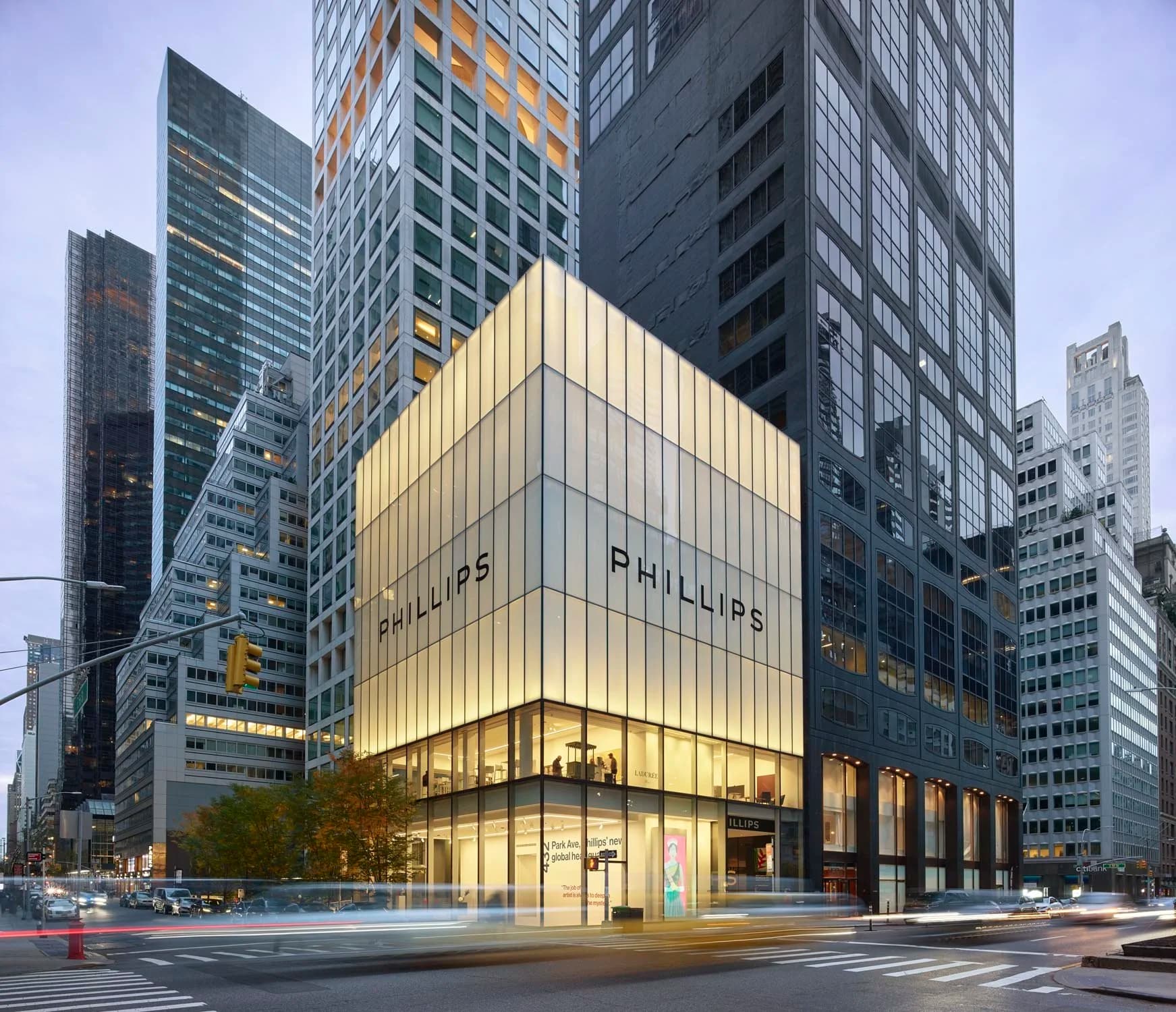 A modern, illuminated building on a city street corner with "PHILLIPS" on the facade, surrounded by tall skyscrapers and moving cars.