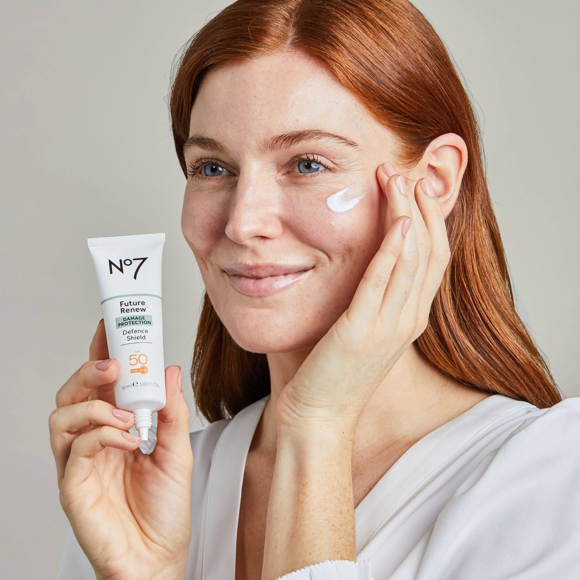 model smiles holding No. 7 facial moisturizer