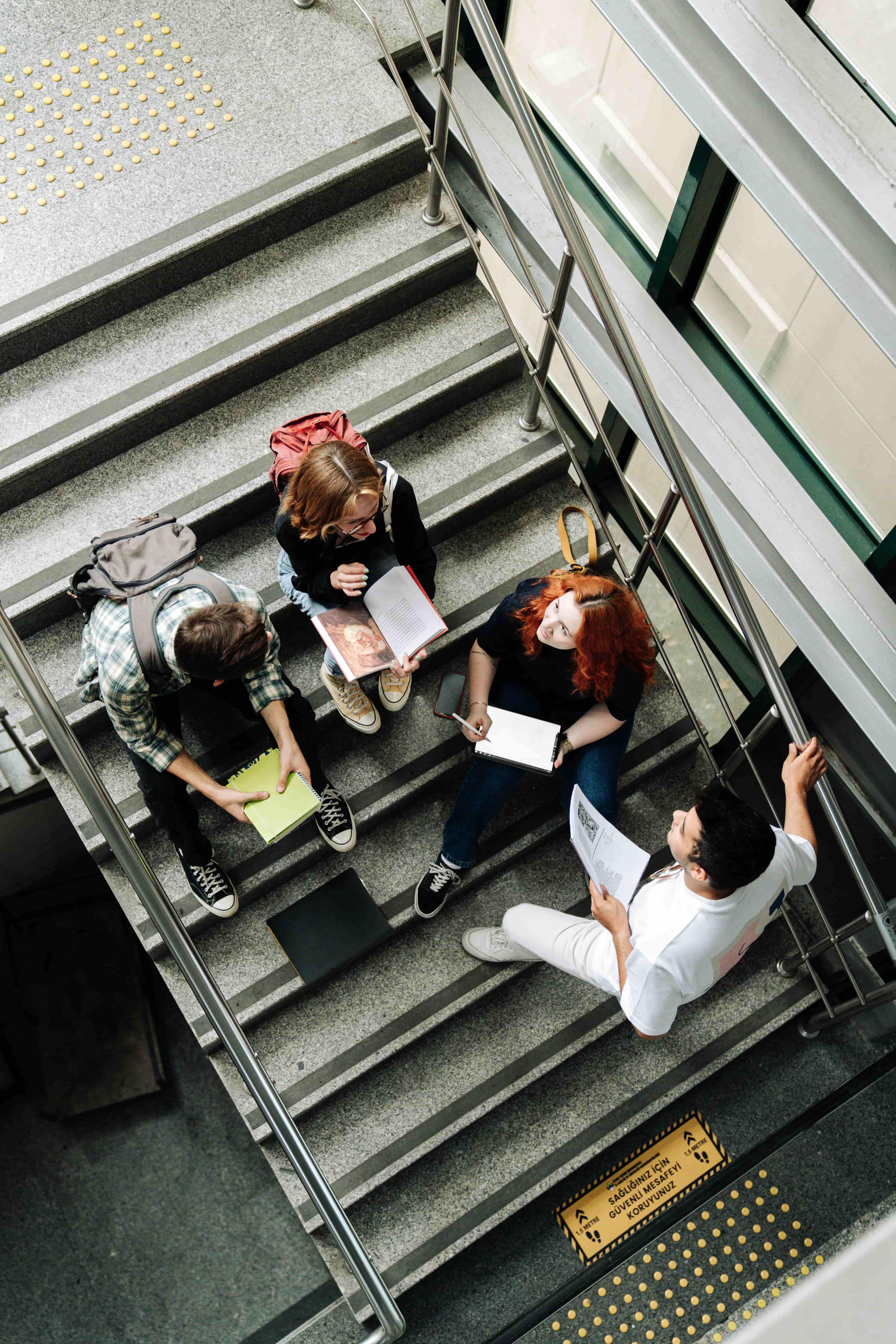 Kids sitting in a school stairway, talking, studying, and reading